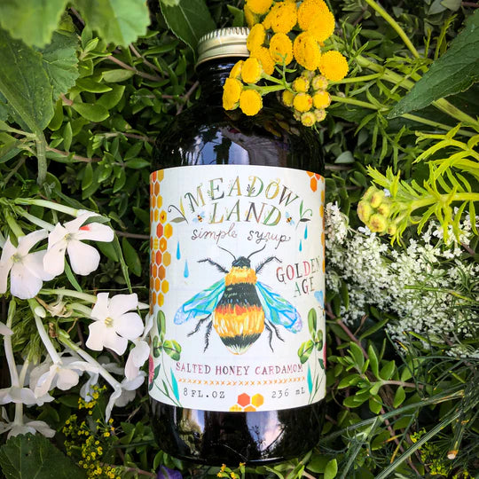 Bottle of Meadowland Salted Honey Cardamom syrup with a bee illustration on a floral background